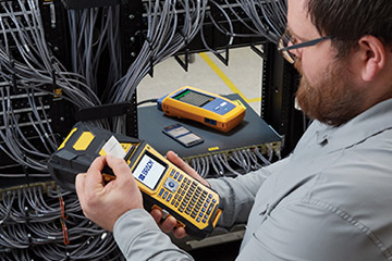 un hombre usando LinkWare Live y una impresora portátil para organizar un complejo conjunto de cables.