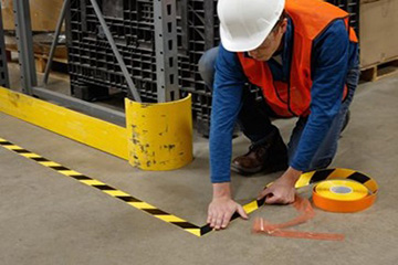 Un trabajador marcando un área de una planta de manufactura con cinta de rayas negras y amarillas striped tape.