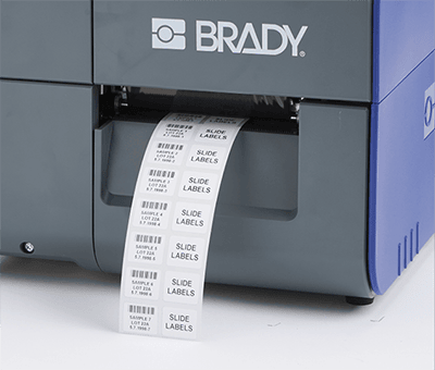 Etiquetas impresas saliendo de una impresora Brady i7500 sin que se vea material de etiqueta desperdiciado.