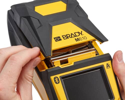 Una persona abriendo una impresora Brady M610 para cambiar el material de etiqueta.