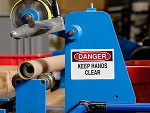 Una etiqueta de seguridad que dice "Danger, keep hands clear" adherida a una pieza de maquinaria industrial.