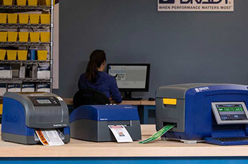 Three different Brady label printers showcasing safety labels in an office environment.