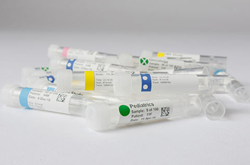 Lab specimen tubes lay in a pile, each with unique label color codes that have been applied with a laboratory label printer.