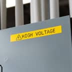 Una etiqueta Brady amarilla grande con el texto &quot;High Voltage&quot; aplicado a un panel eléctrico.