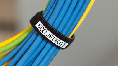 Un manojon de cables de color azul, verde y amarillo envueltos con una correa de velcro negra que tiene una etiqueta blanca.