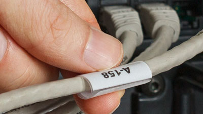 Una mano agarrando una etiqueta de identificación blanca enrollada alrededor de un cable gris.