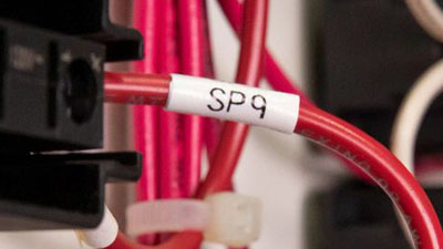 Un cable rojo dentro de un panel identificado con una etiqueta blanca.