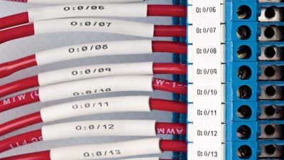 Una serie de cables rojos con mangas termocontráctiles de identificación dentro de un bloque terminales.