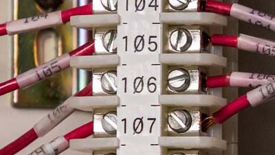 Ocho alambres rojos identificados con una etiqueta de bloque de terminal blanca y etiquetas envolventes individuales.