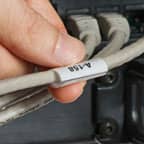 Una persona sosteniendo una etiqueta envolvente aplicada a un cable gris.