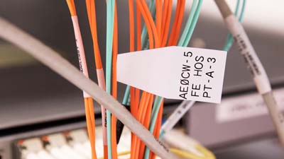 Una etiqueta Quick Flaf de Brady que se extiende desde un cable, entre un grupo más grande de etiquetas, con texto impreso para identificarla.