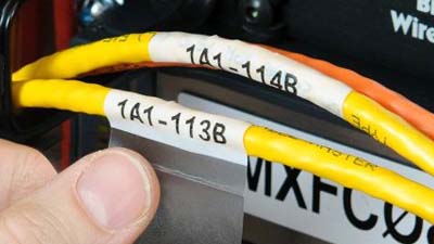 Un técnico aplicando una etiqueta autolaminable Brady con el texto 1A1-1138 a un cable.