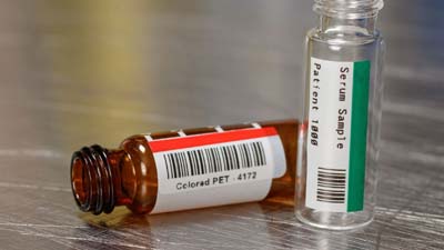 Dos viales con etiquetas de poliéster de color rojo y verde.