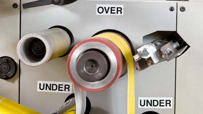 Varias etiquetas de vinilo para todo clima de Brady con el texto OVER y UNDER aplicado a una máquina troqueladora para indicar la dirección en la que se debe enhebrar el material.