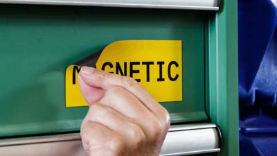 Una muestra del material de etiqueta de poliéster magnético de Brady con el texto MAGNETIC impreso adherido magnéticamente a la cubierta metálica de un equipo.