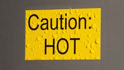 Una etiqueta Brady Toughwash amarilla con el texto CAUTION HOT impreso en ella. La etiqueta está húmeda como si la hubieran rociado recientemente para limpiarla.