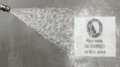 Un trabajador utiliza un chorro de agua para limpiar una etiqueta detectable de metal Brady Toughwash que está aplicada a una pieza de maquinaria.