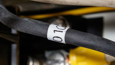 Una etiqueta envolvente Tedlar blanca autoextinguible con texto negro aplicado alrededor de un cable negro de una caja eléctrica.