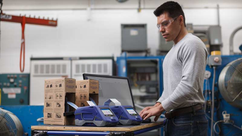 Un hombre en un almacén está haciendo etiquetas termocontráciles en una impresora de etiquetas M611 Brady.